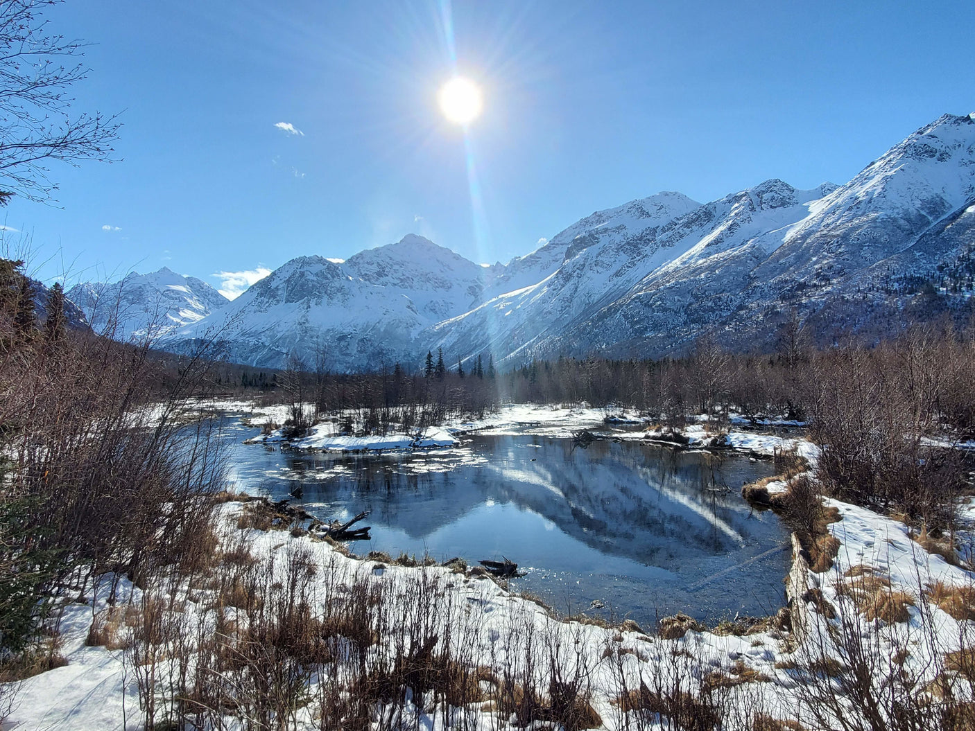 Experience winter's beauty! Sunny, snow-capped mountains reflect in a calm river. An RV rental is ideal for exploring such scenic views.