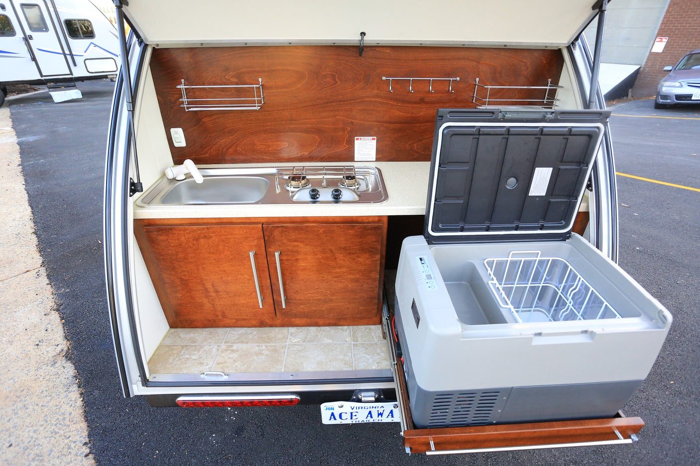 A convenient rv rental outdoor kitchen featuring a sink, two-burner stove, cabinetry, and a pull-out refrigerator.