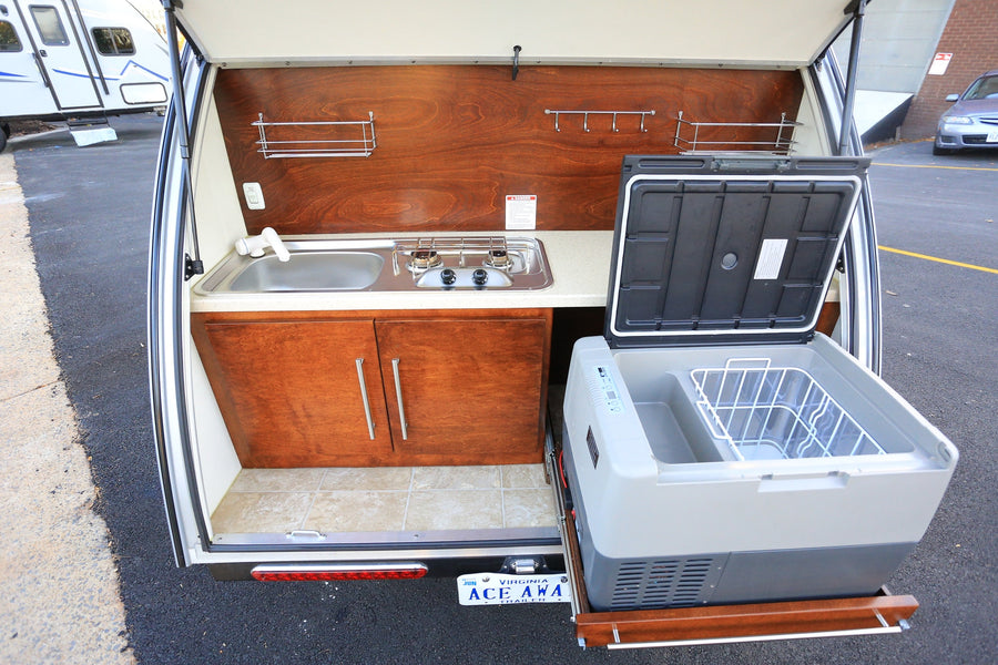 A convenient rv rental outdoor kitchen featuring a sink, two-burner stove, cabinetry, and a pull-out refrigerator.