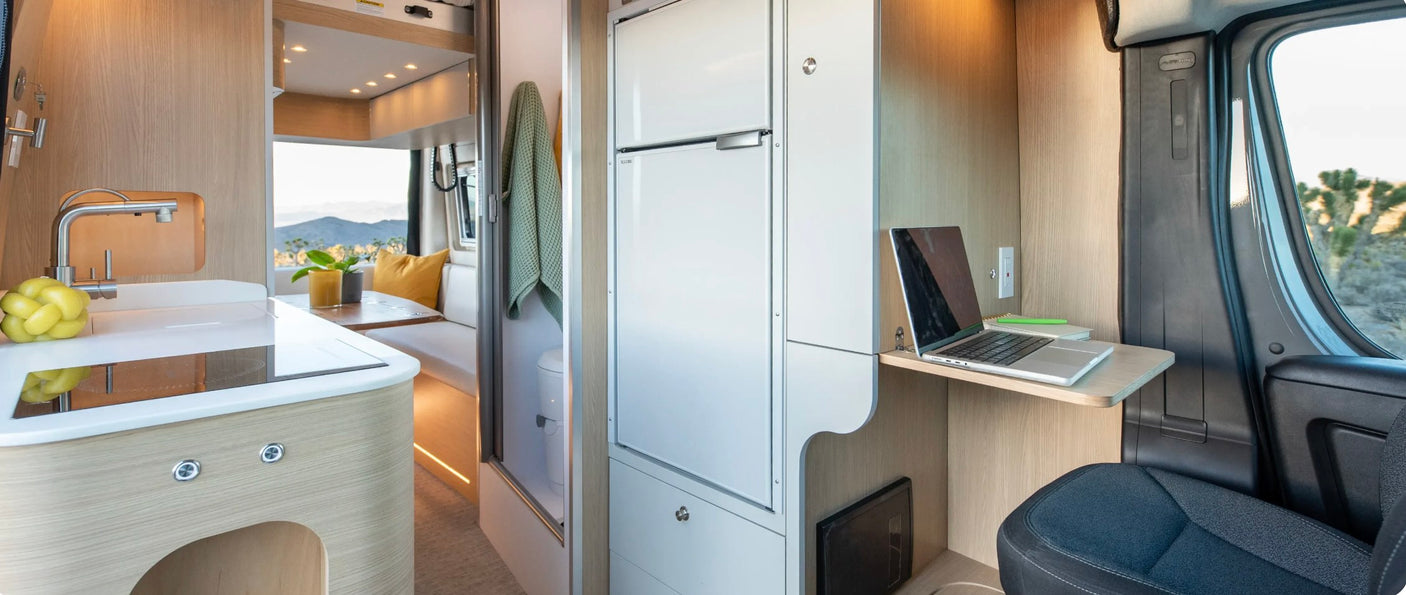 Bright RV rental interior showcasing a kitchen, desk with laptop, fridge, and dining space. Ideal for remote work travel.