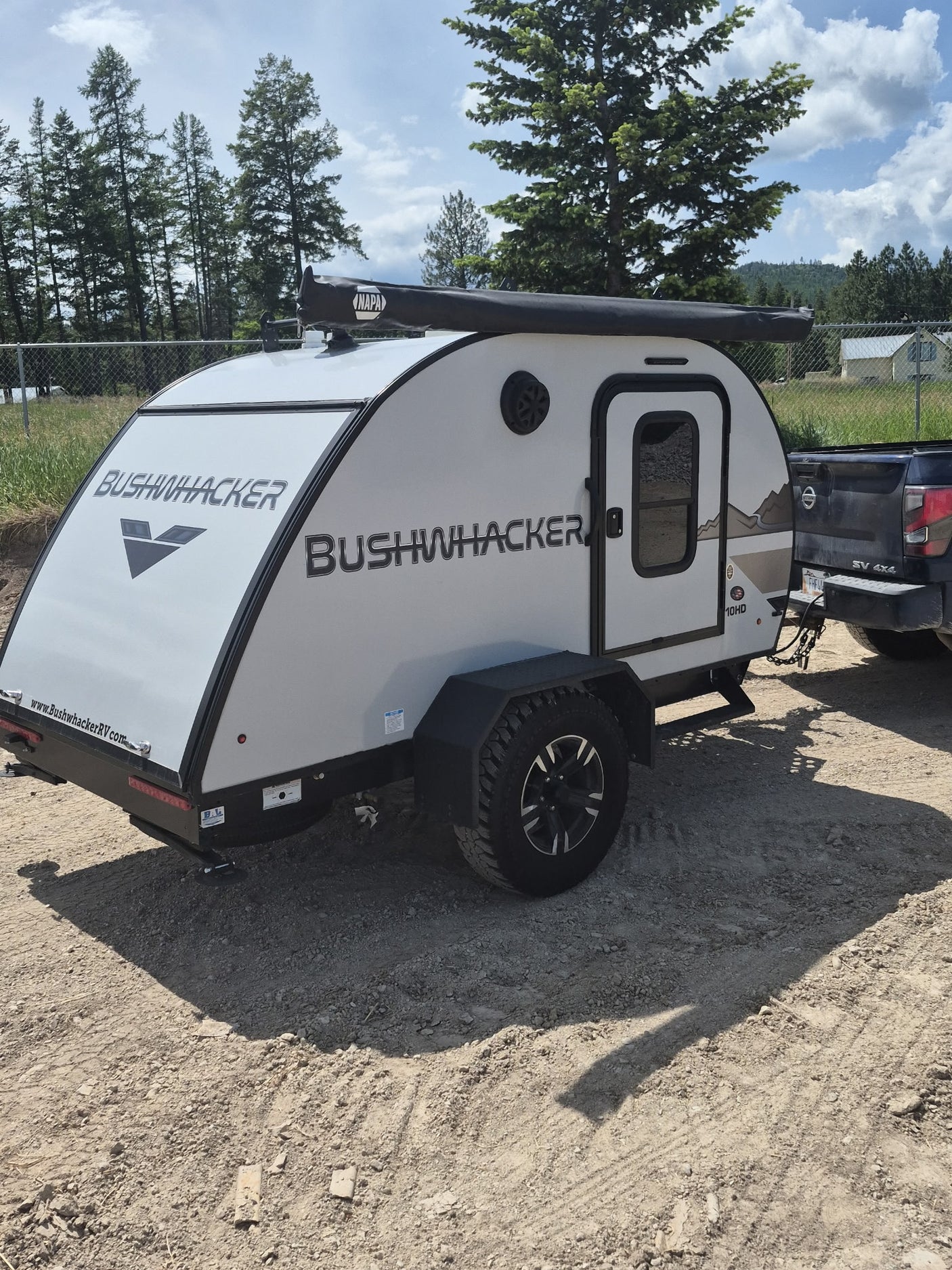 ready for adventure on a dirt road.|Off-road teardrop RV rental: A white Bushwhacker 10HD trailer hitched to a Nissan truck