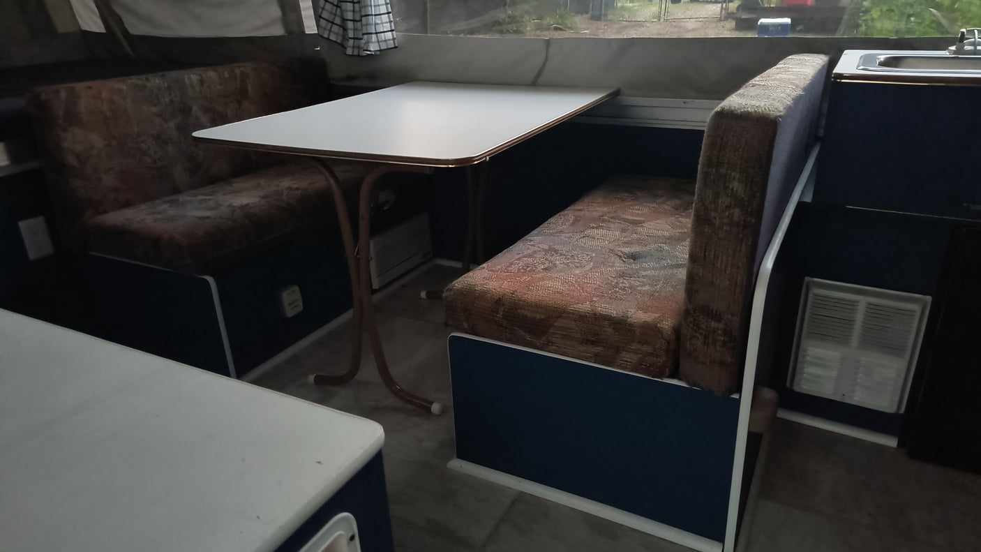 RV rental camper: Cozy dinette with patterned benches & white table. Sink visible, ready for your road trip.