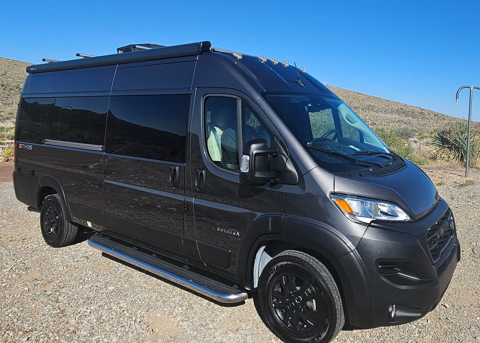 parked in a sunny desert with mountains behind.|Dark grey camper van