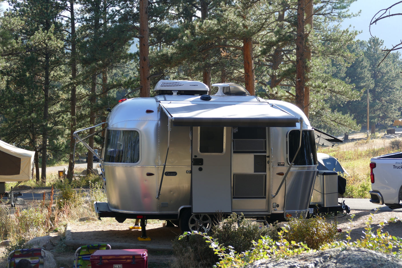 A sleek silver Airstream Caravel rv rental is set up at a sunny, wooded campsite, offering comfortable outdoor living.