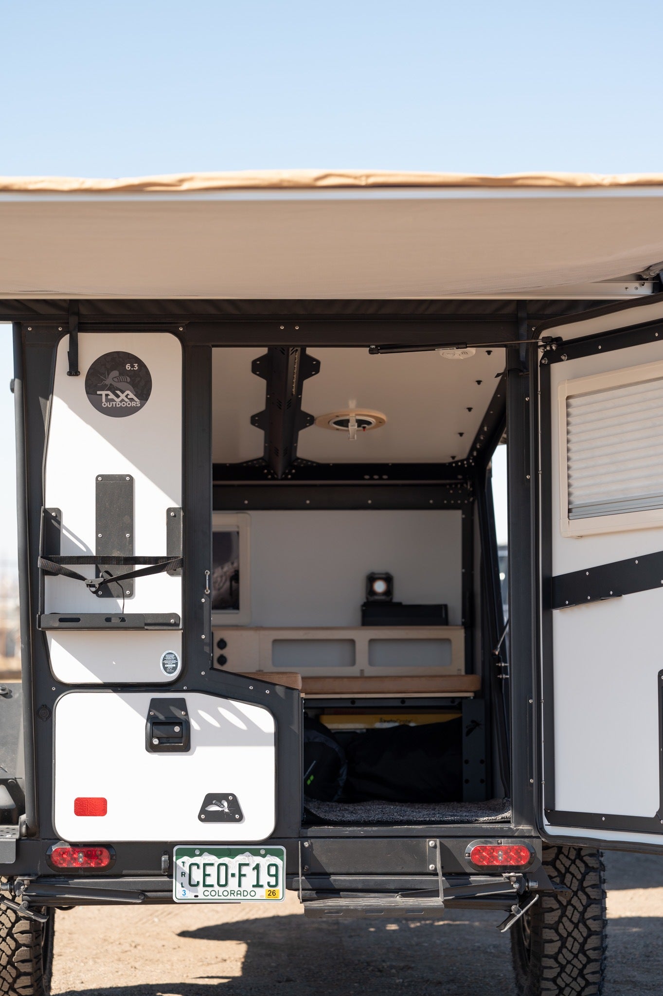 Open rear hatch of a TAXA Outdoors camper, an ideal rv rental for adventure. Shows organized mobile living space.