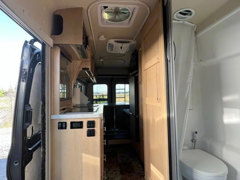 RV rental interior: From the open side door, see the compact kitchen area, appliances, and integrated wet bath.