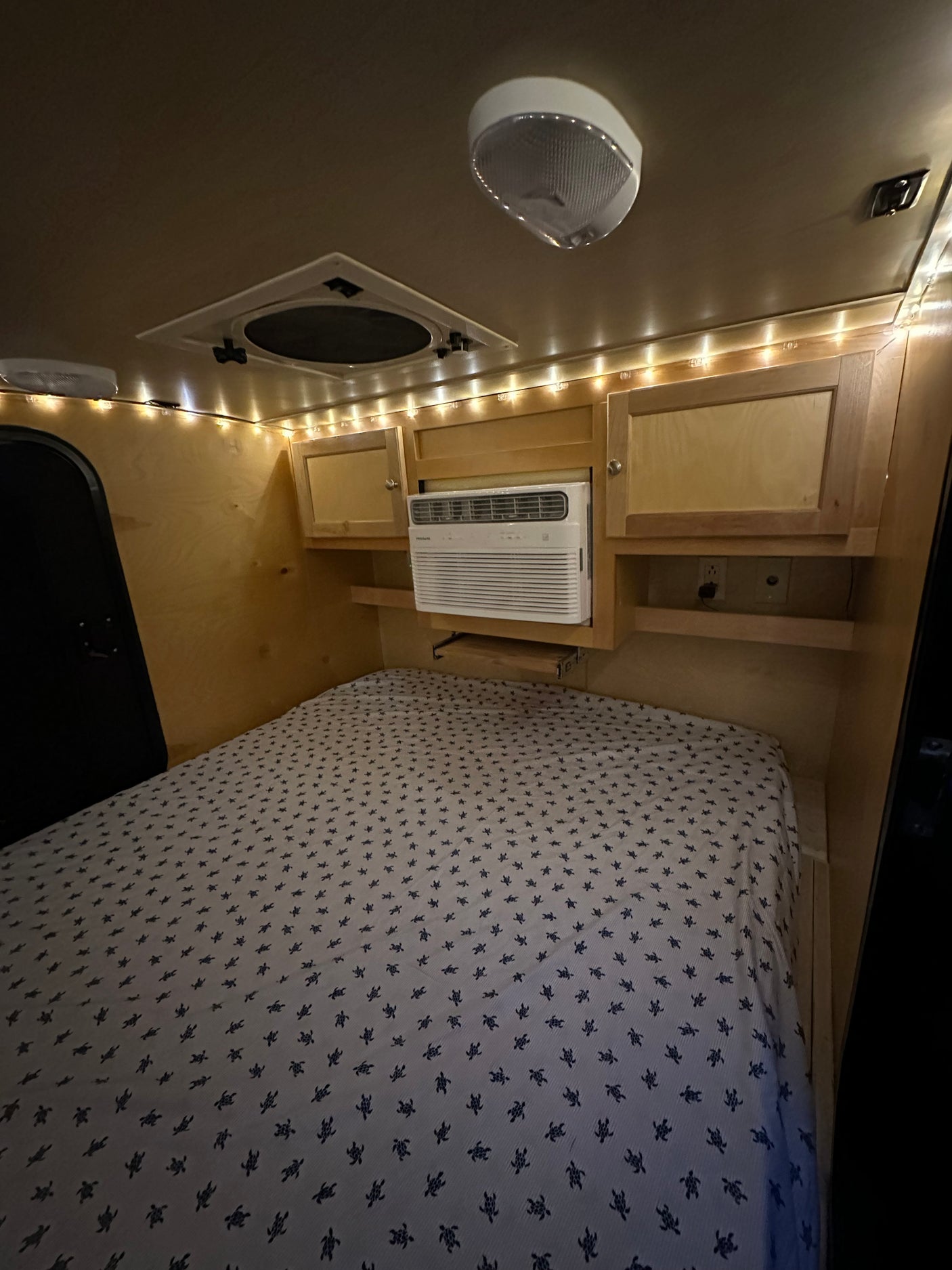 Comfortable RV rental interior featuring a bed with turtle-patterned sheets, AC unit, and ambient string lights.