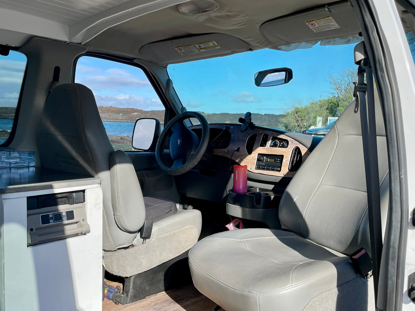 RV rental: Bright interior featuring a dashboard, grey seats, and a stunning water view from the front. Ready for adventure.