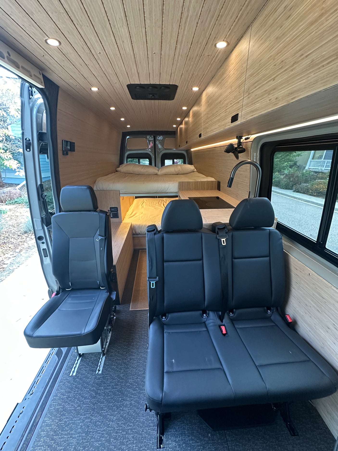 Modern rv rental camper van interior featuring versatile seating, full kitchen, and cozy bed in wood paneling.