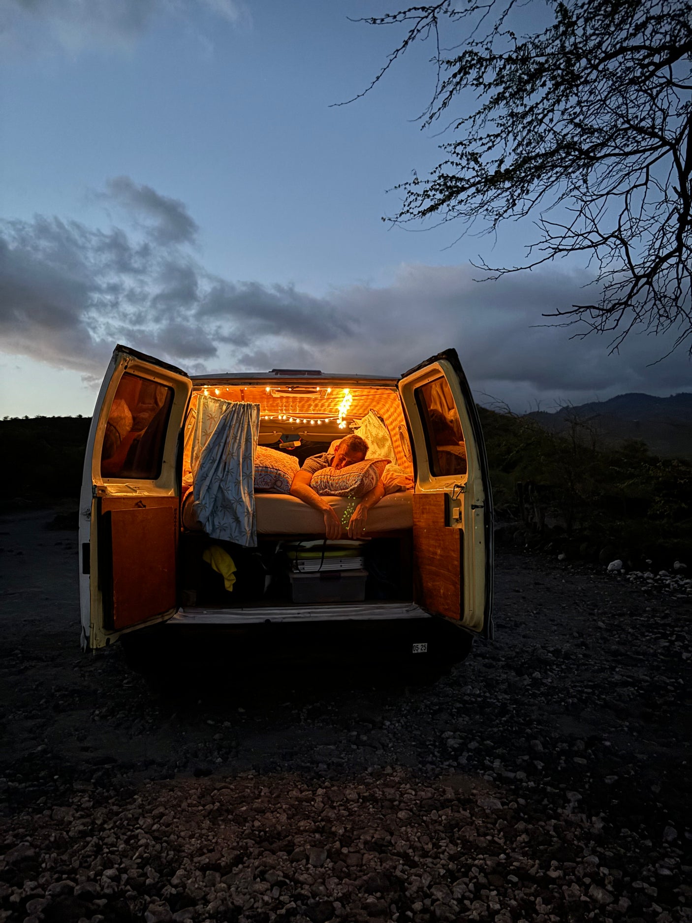 Person sleeping in a cozy, lit **rv rental** campervan at night, parked outdoors under a cloudy sky.