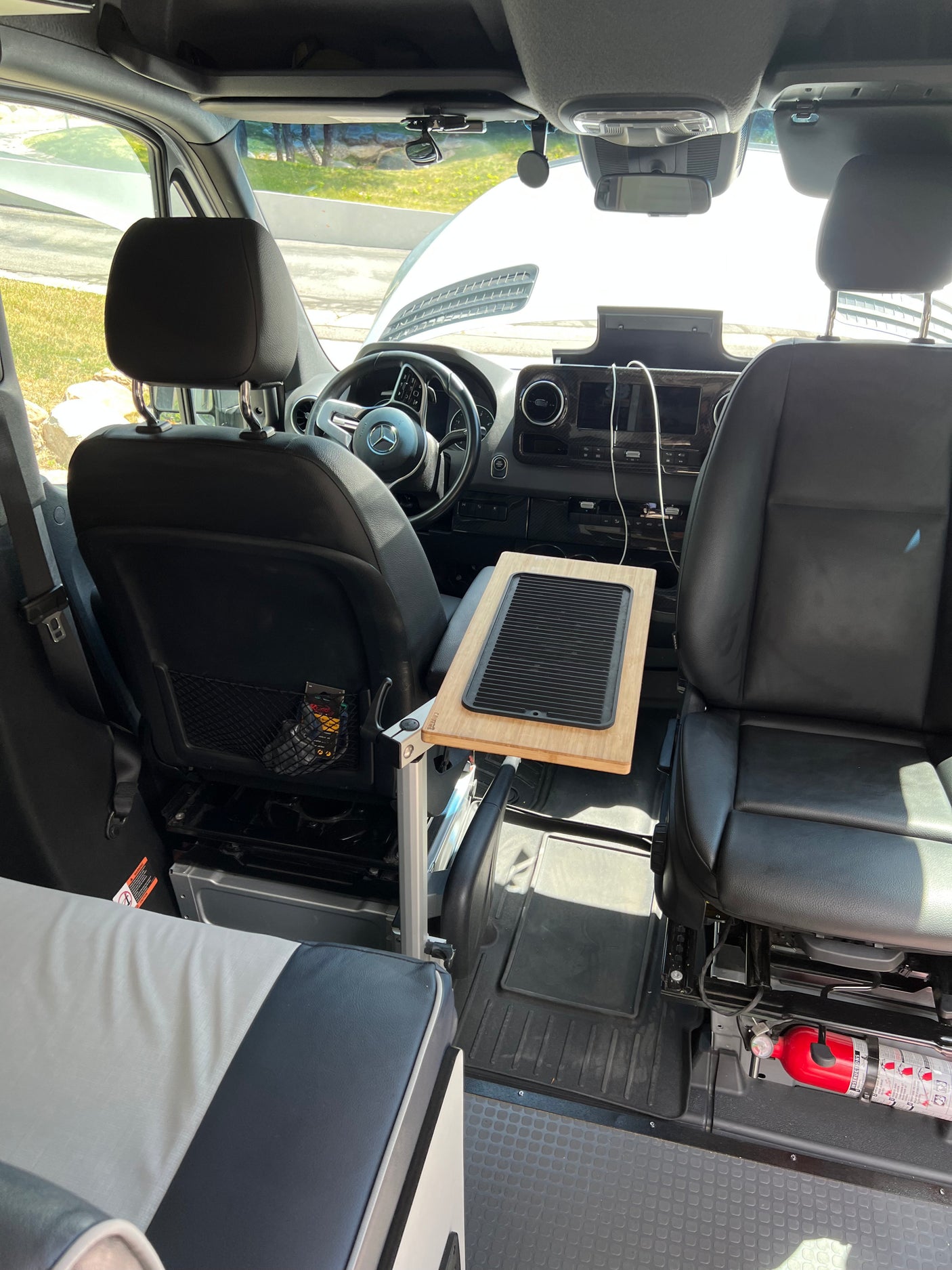 Inside this RV rental: front seats, dashboard, and a convenient table with a black insert for camper van trips.