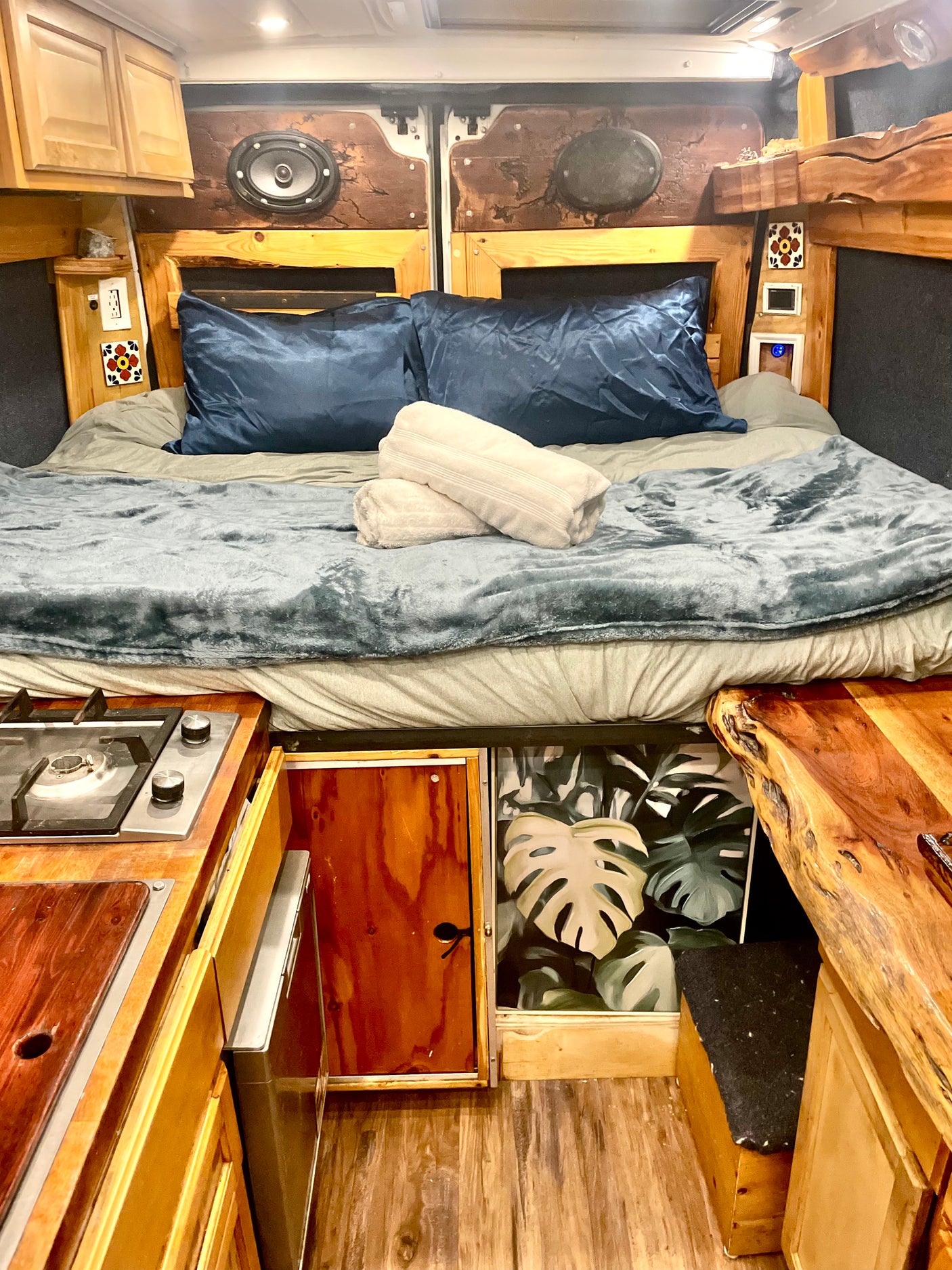 Experience van life in this cozy rv rental, featuring a comfortable bed, compact kitchen, and natural wood details.