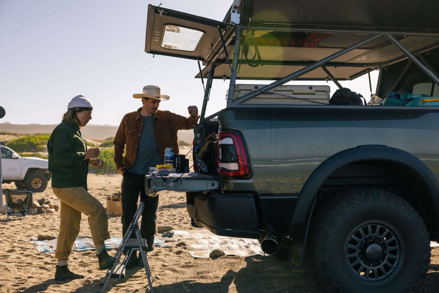 RV rental for overlanding: Two people by their truck camper on a sandy beach, setting up camp.