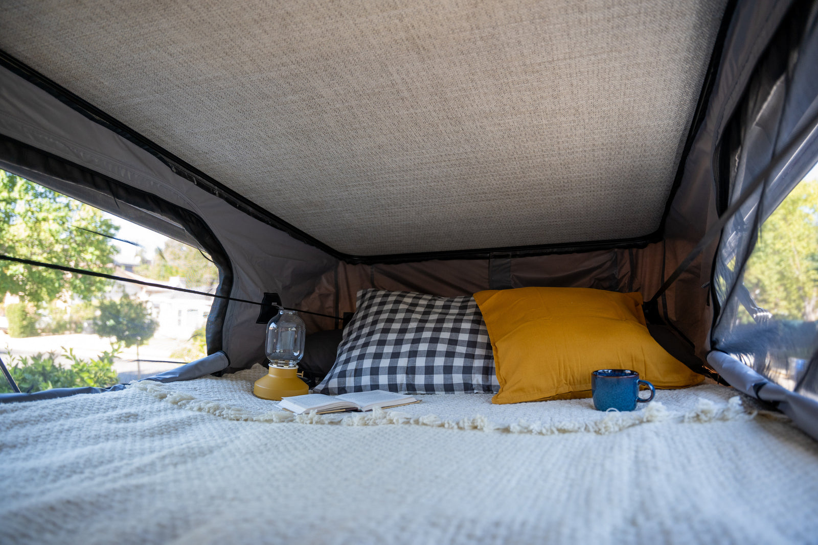 Cozy RV rental interior with comfy bed, pillows, book, and lantern. Perfect for a comfortable glamping adventure.