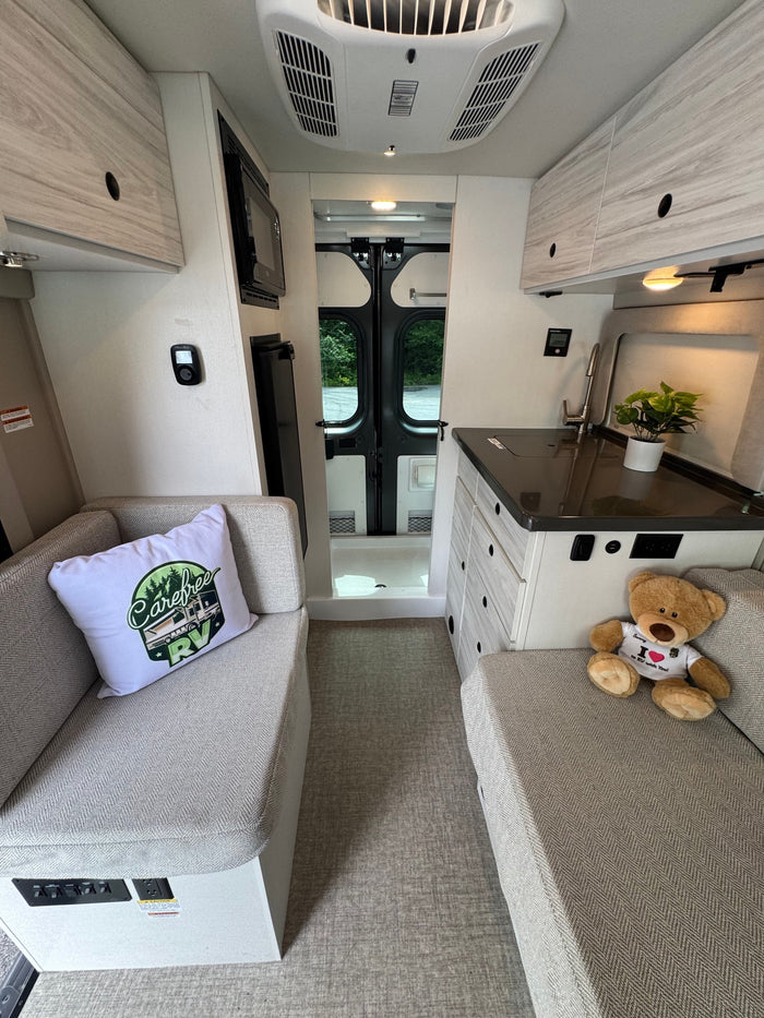 Cozy RV rental interior with light wood finishes, a compact kitchen, comfortable seating, and rear doors for scenic views.