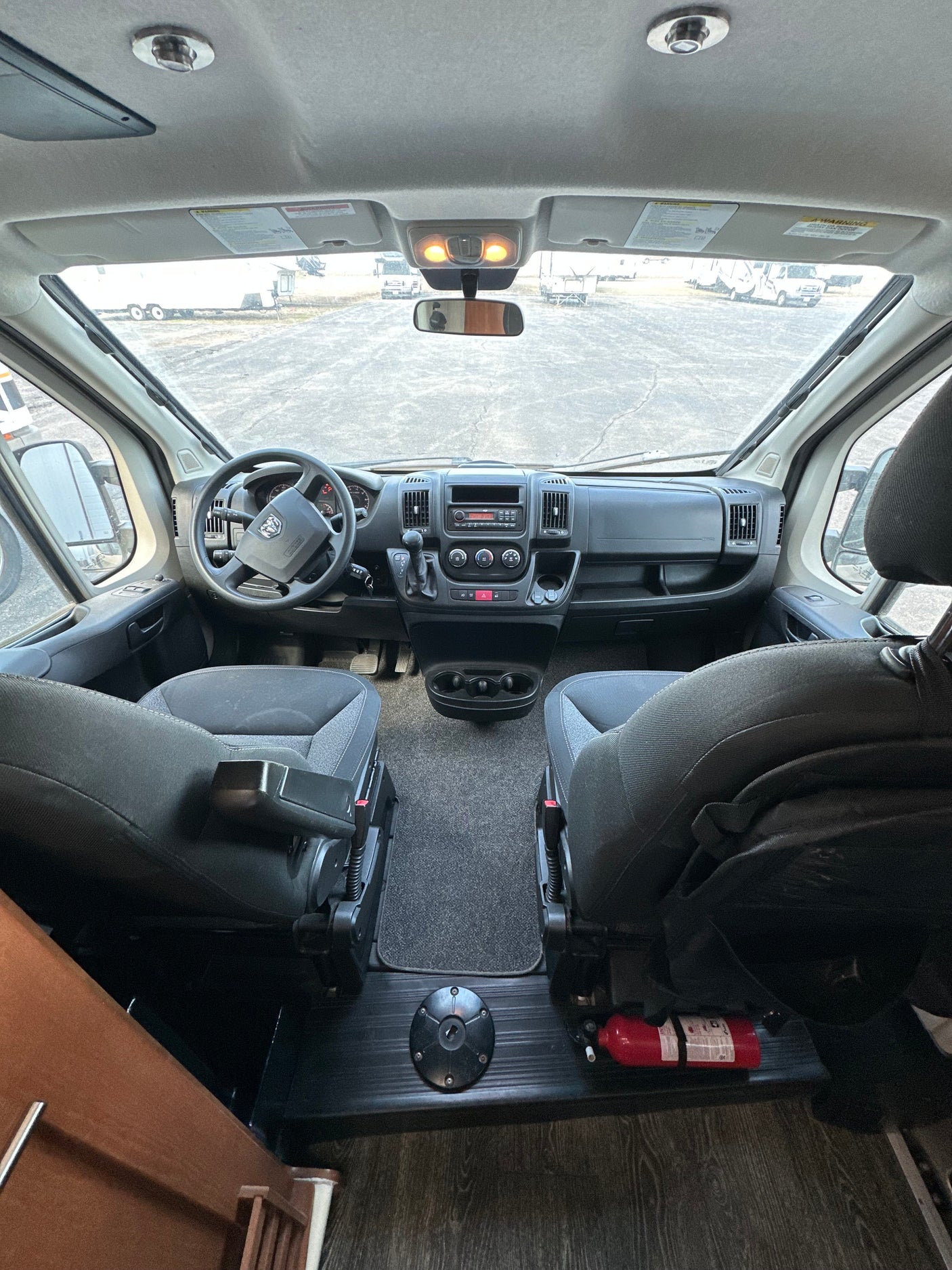 Interior view of an RV rental showing the dashboard, steering wheel, and both front seats. A fire extinguisher is on the floor.