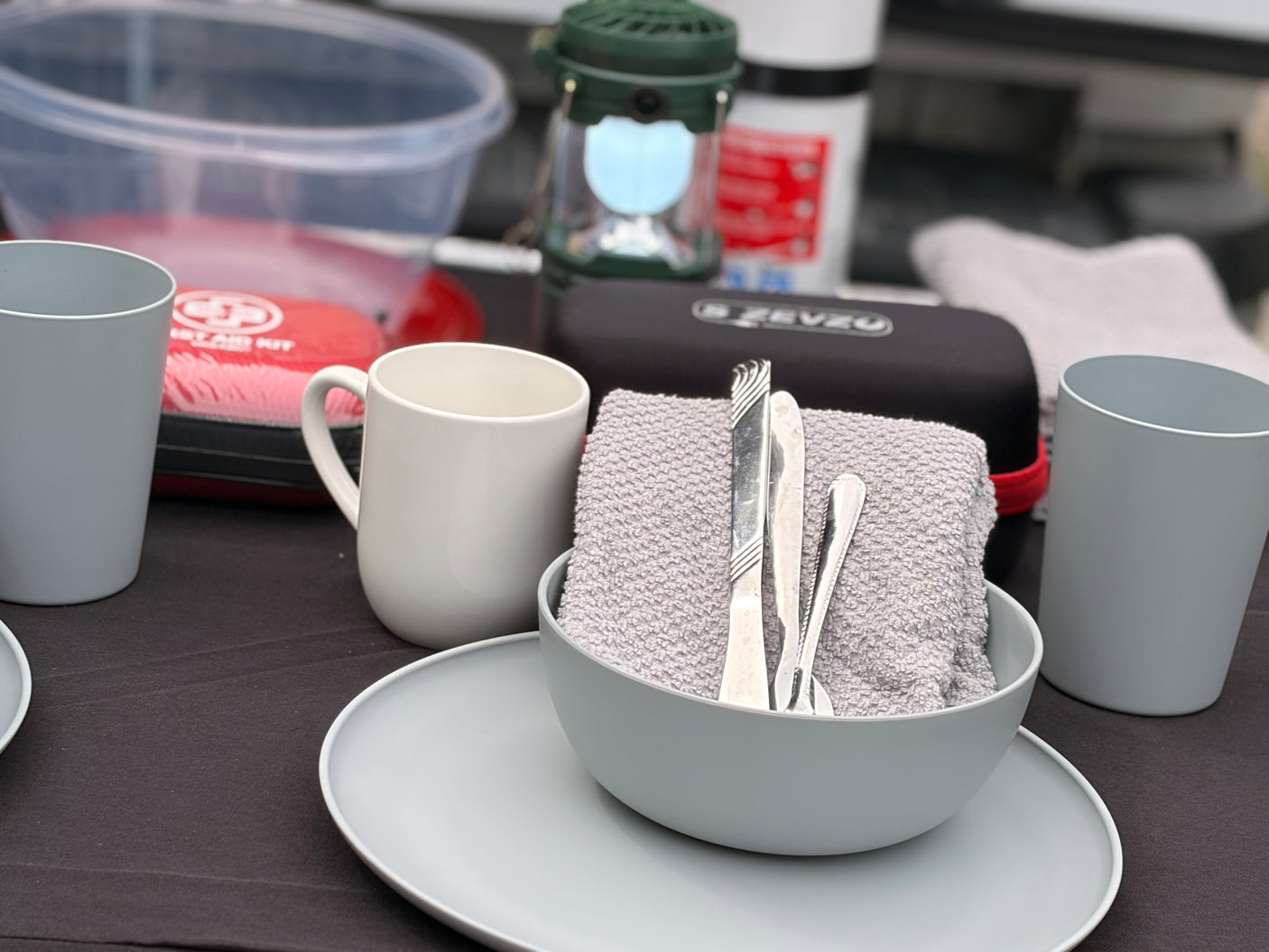 RV rental essentials: table set with grey dishes, silverware, first aid kit, and lantern, ready for camping.