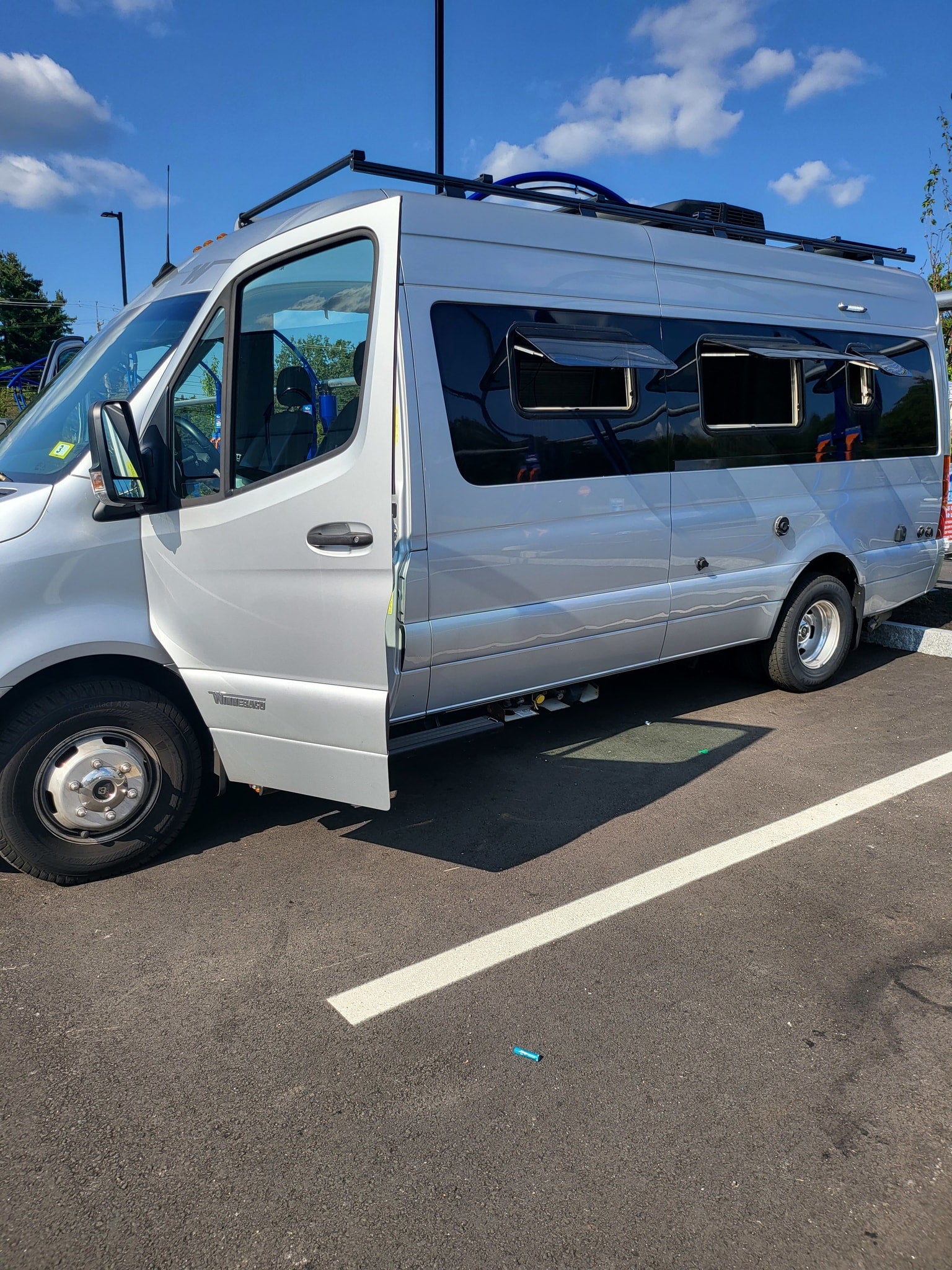 Silver Winnebago camper van, perfect for an RV rental, with its driver's door open in a parking lot.