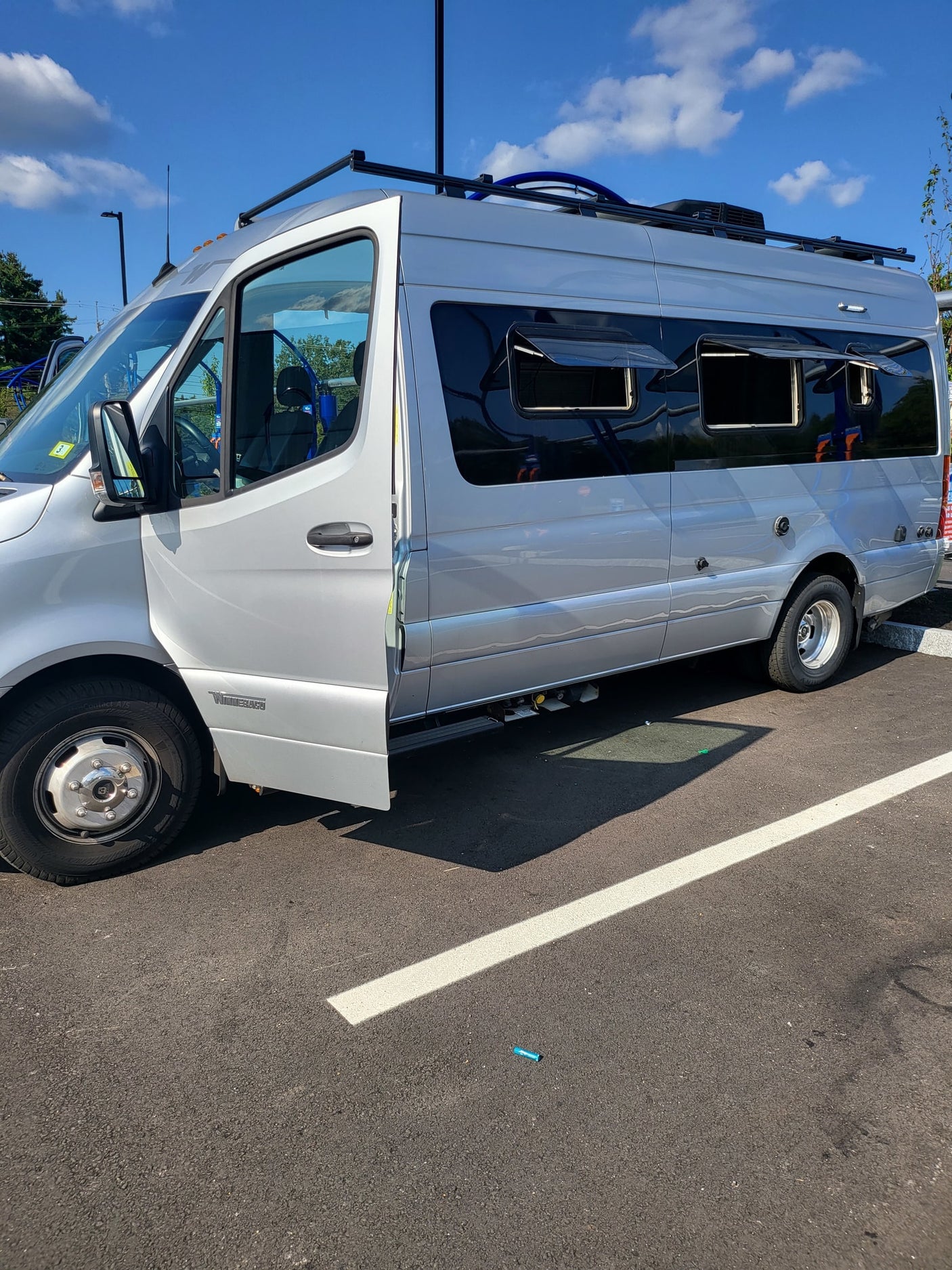 Silver Winnebago camper van, perfect for an RV rental, with its driver's door open in a parking lot.
