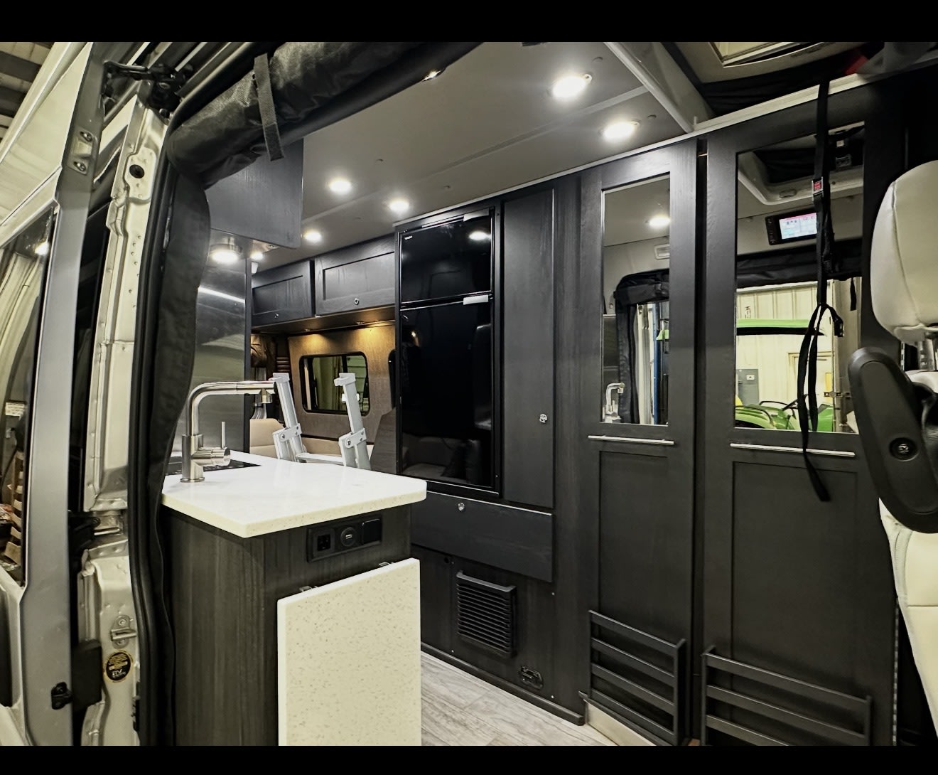 Inside a modern rv rental: a sleek kitchenette with sink, dark cabinetry, and built-in refrigerator. Ready for your journey. — photo 11
