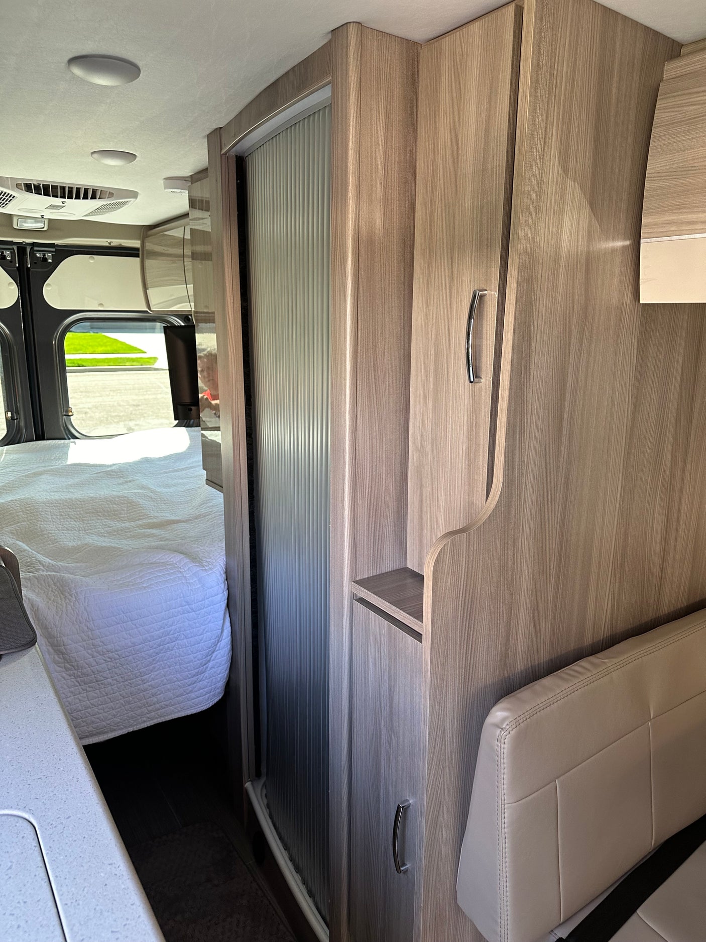 Inside this RV rental, discover a comfortable interior with a white bed, wood-paneled storage, and a sleek counter.