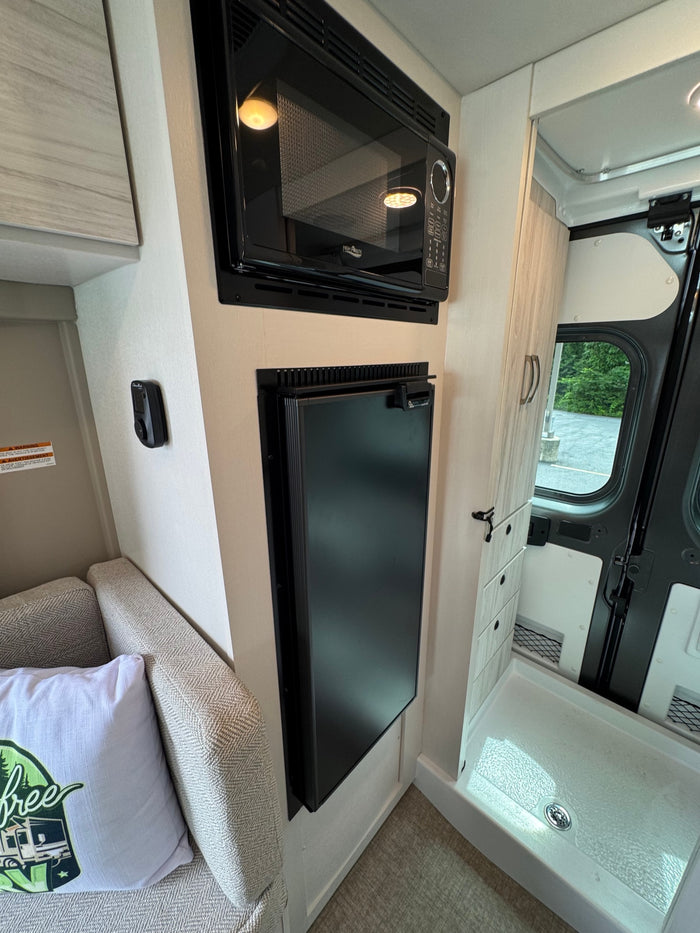 Inside a modern RV rental: sleek microwave, tall refrigerator, and integrated shower. Efficient use of space.