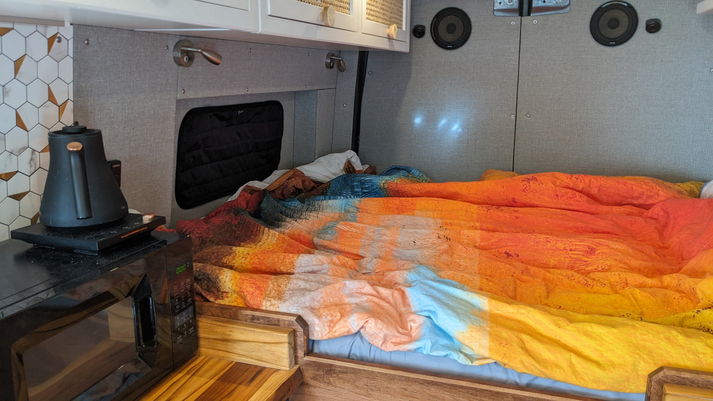 Cozy RV rental interior: a vibrant bed, kitchen with microwave & kettle, perfect for compact van adventures.