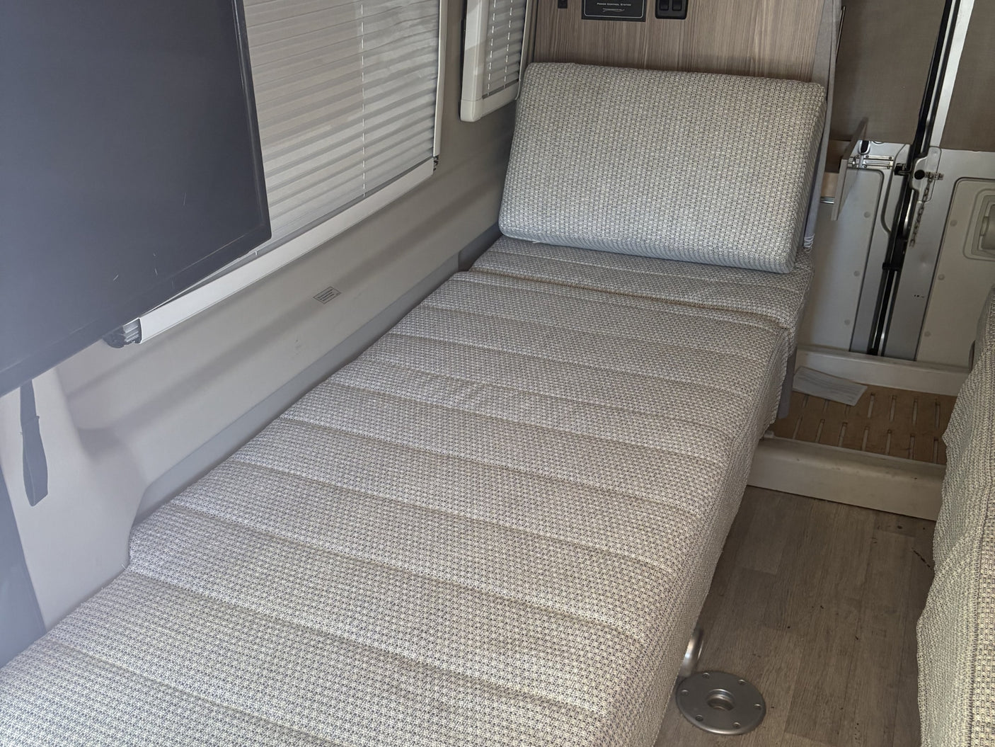 RV rental: Interior view of a functional sleeping/lounge area with patterned cushions, TV, and window blinds.