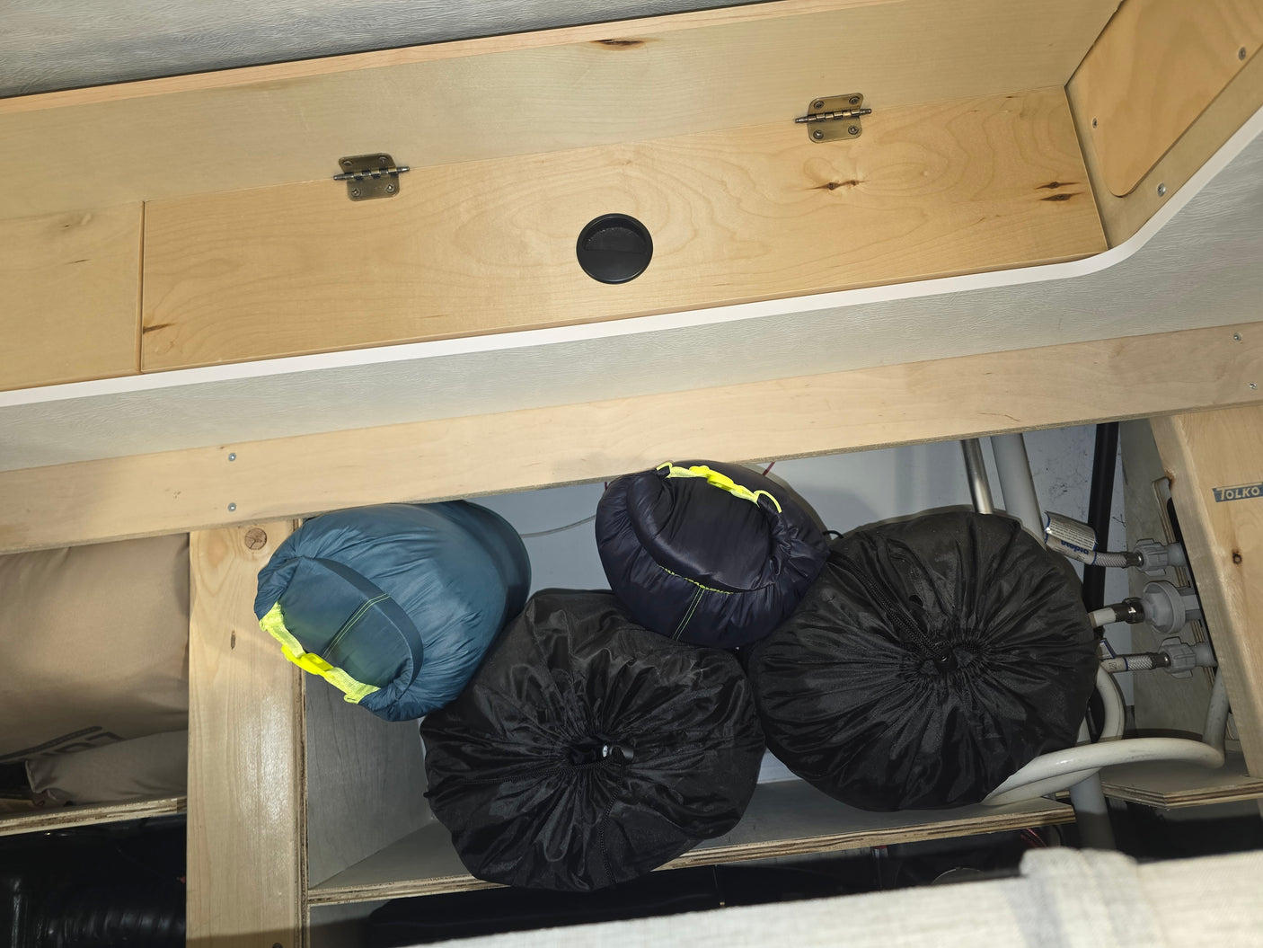 RV rental: Organized camper storage showing packed sleeping bags and gear in a wooden cabinet, with utility plumbing visible, providing essential context.