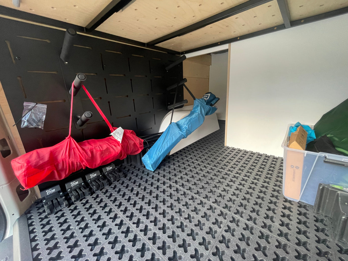 Optimized RV rental cargo: Camper van with modular floor mats, wall-mounted gear racks holding rolled items like chairs.