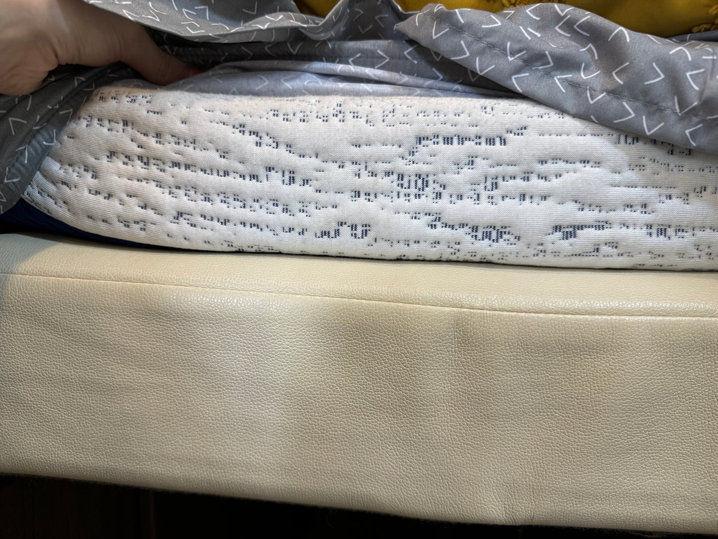 RV rental interior comfort: Hand holds grey patterned fabric above a white quilted blanket & cream seating cushion.
