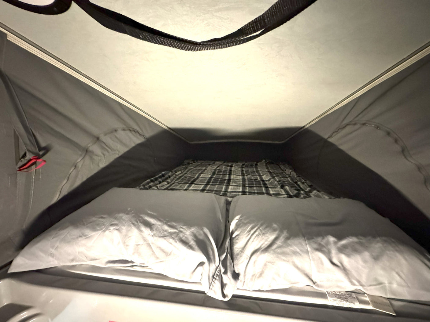 Interior view of a cozy pop-top RV rental bed, featuring light pillows and a plaid blanket, ready for sleeping.