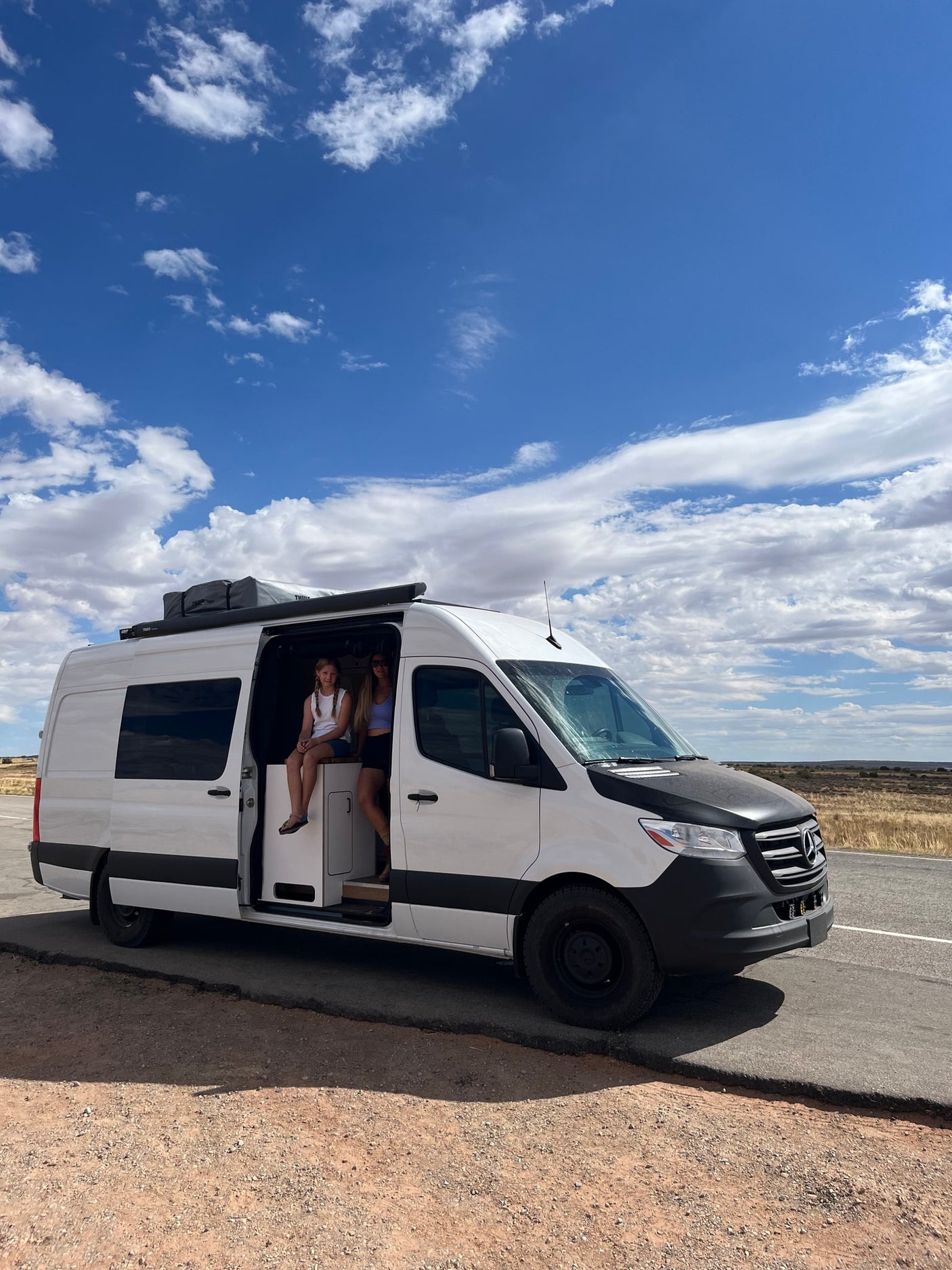 Embark on a road trip adventure! This RV rental, a white travel van, is parked with two people enjoying the view from its open side door.