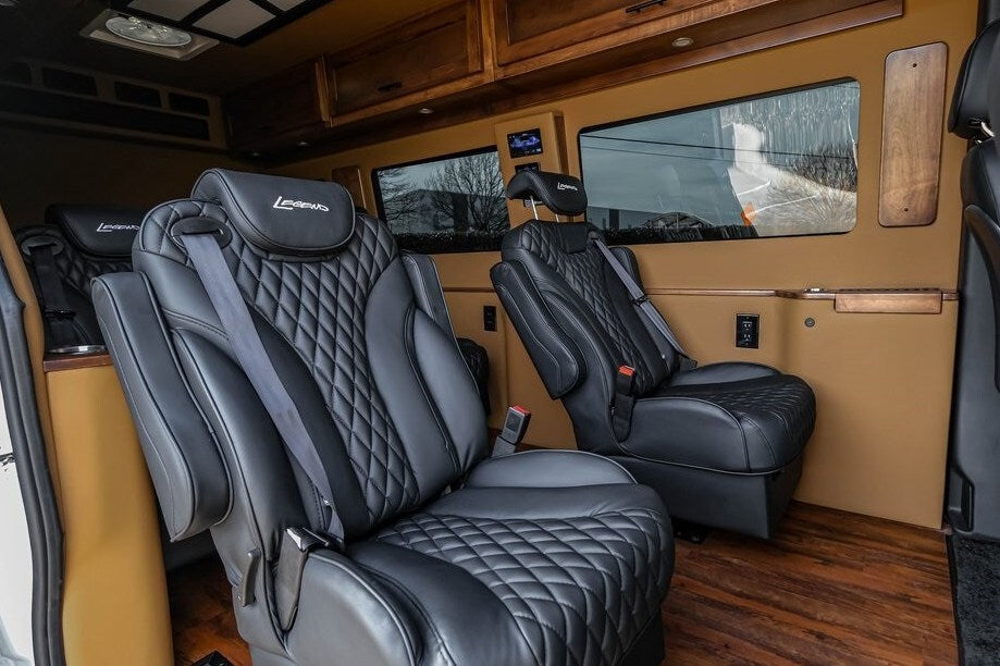 Plush RV rental interior features black diamond-stitched captain's chairs with "Legends" headrests, wood cabinets, and flooring. — photo 11
