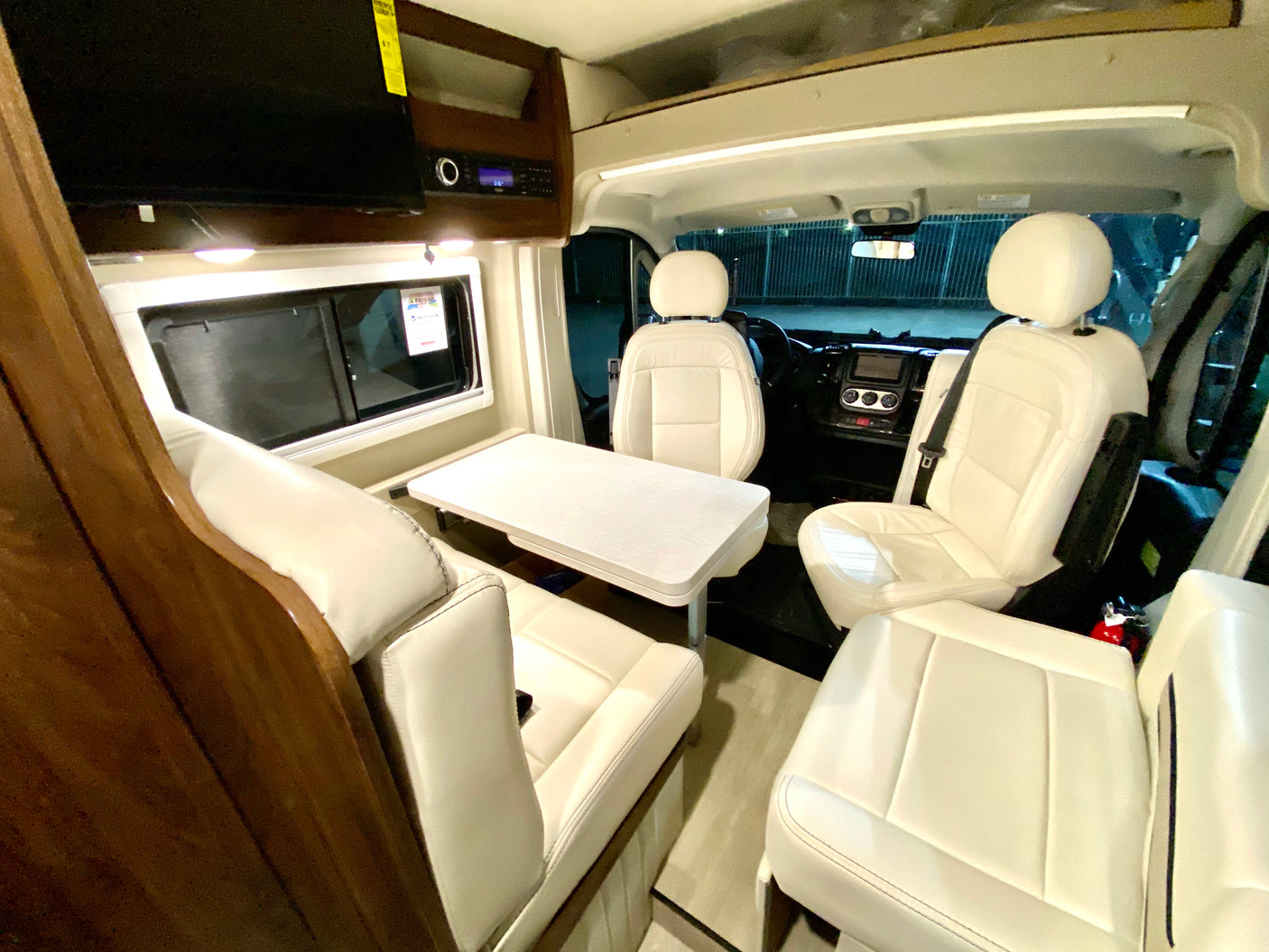 Spacious RV rental interior with white leather seating, a dining table, and a view of the driver's cockpit.