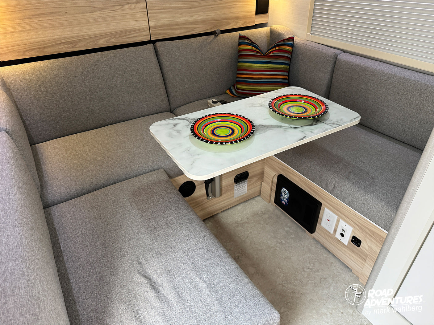 Relaxing rv rental lounge: Gray L-shaped dinette, marble table, vibrant dishes, and cozy cushions for comfortable travel.