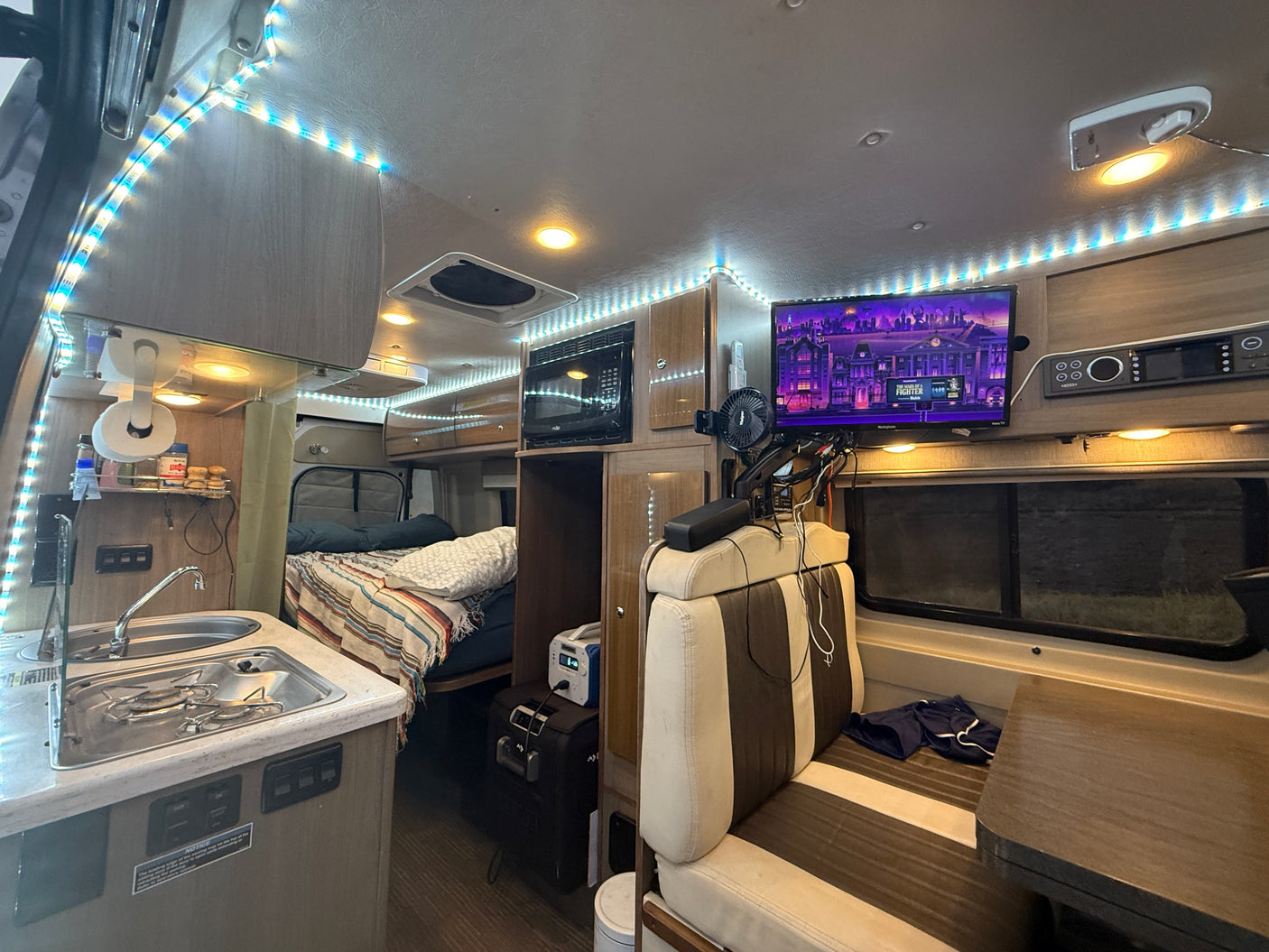 Spacious RV rental interior with kitchen, cozy bed, entertainment TV, & ambient LED lighting for comfortable travel.