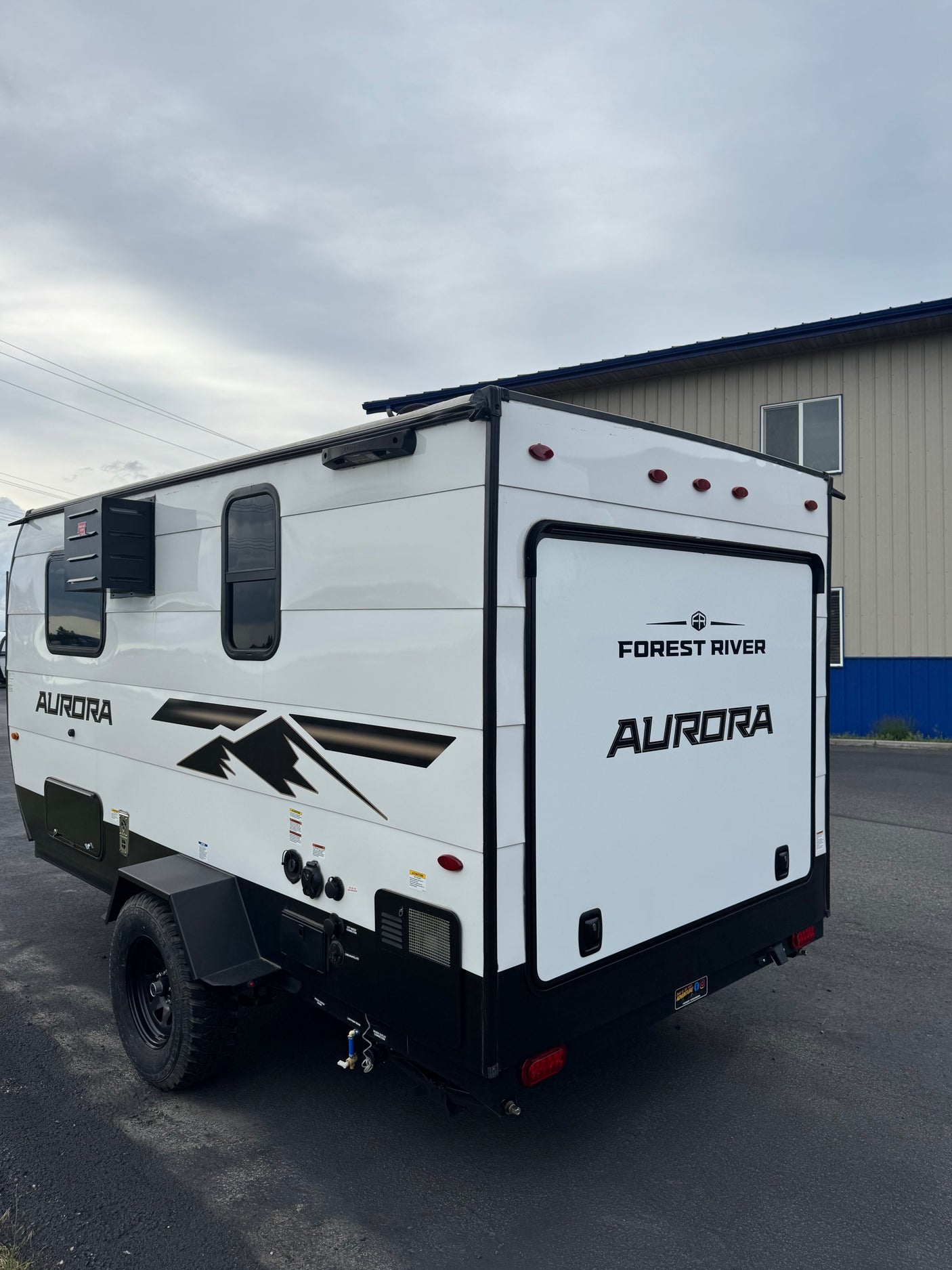 A white Forest River Aurora camper trailer, ideal for your next rv rental adventure. Features black trim, windows, and rugged wheels.