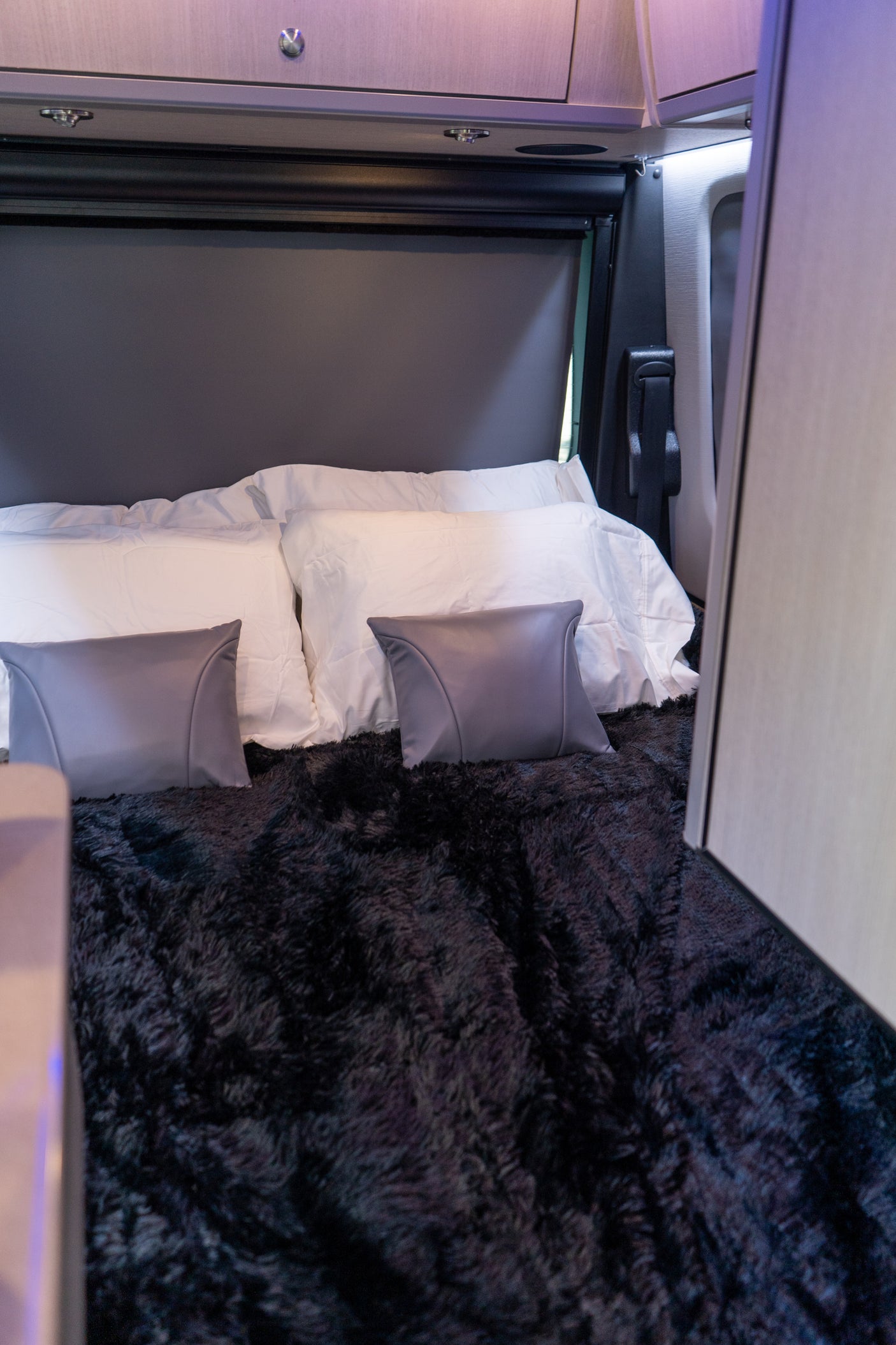 Cozy RV rental interior featuring a comfortable bed with white pillows and a soft, dark, fluffy blanket, ready for a restful night.
