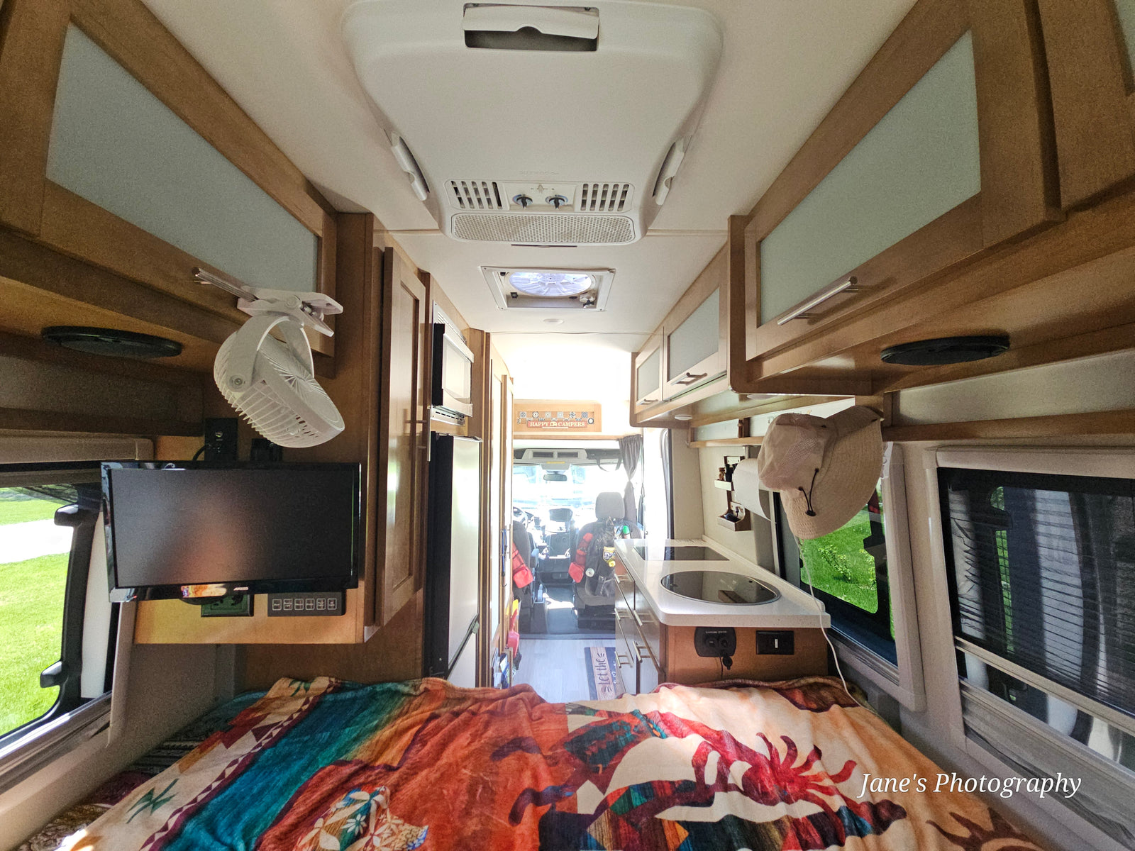 Interior of an RV rental, looking forward from the bed to the kitchenette, overhead cabinets, and driver's cockpit.
