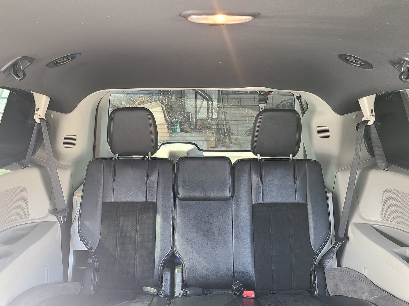 Inside an RV rental: Rear view showcasing two black seats, overhead light, AC vents, and safety belts in a spacious cabin.