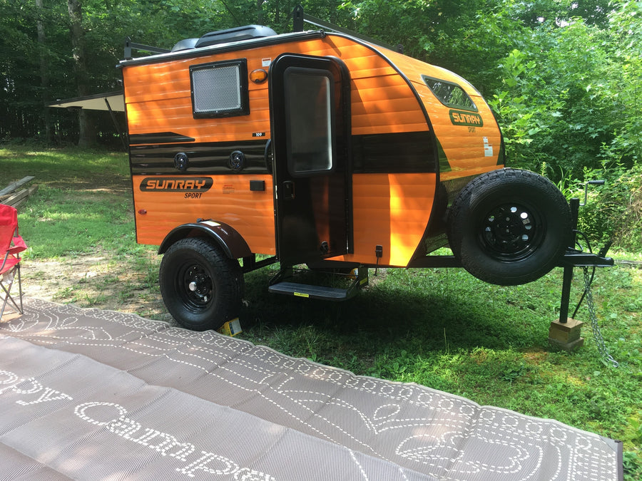 Orange Sunray teardrop camper, an ideal RV rental. Parked on grass at a sunny campsite, ready for adventure!