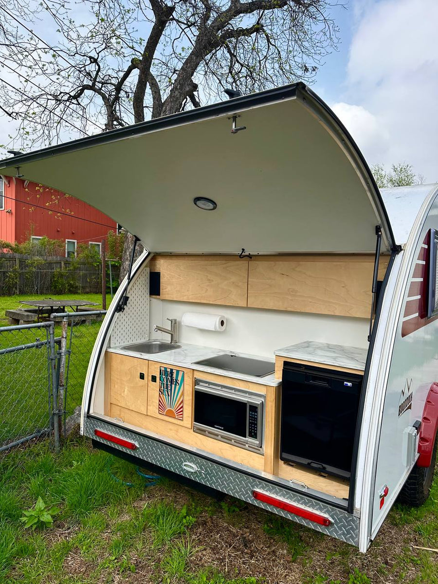 parked under a large tree with sunflowers. Perfect for outdoor adventures!|Compact teardrop RV rental with an open outdoor kitchen