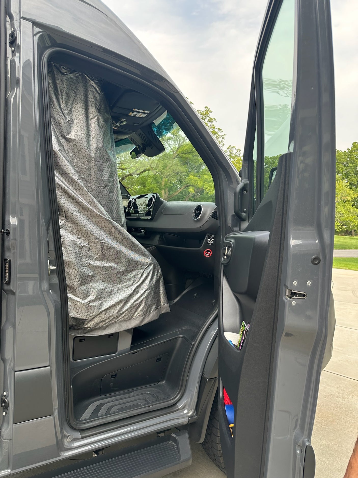 Open driver door of a grey RV rental van with a silver thermal privacy curtain across the windshield.