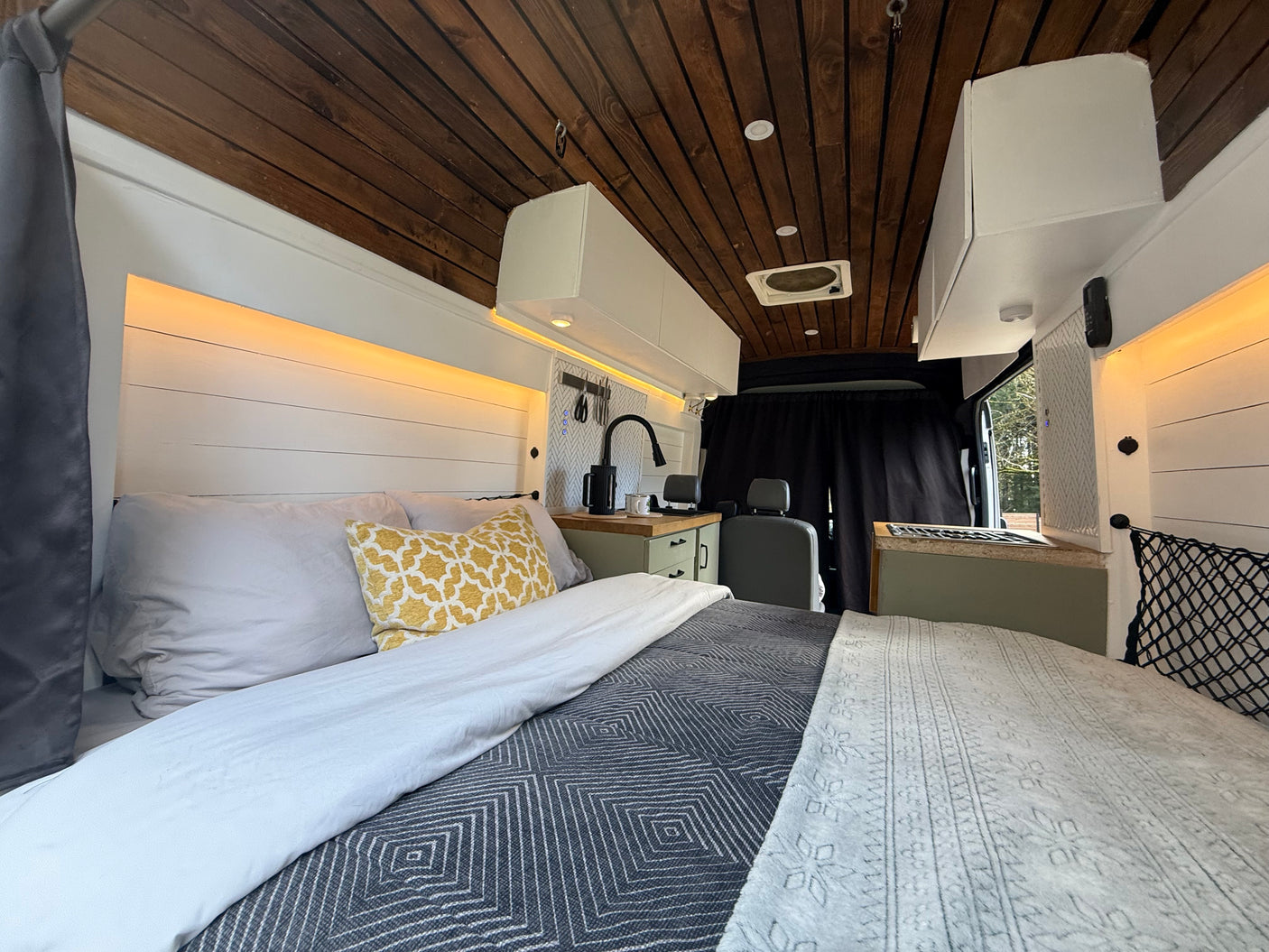 This rv rental's cozy van conversion features a full bed, custom kitchen, wooden ceiling, and practical LED lighting.
