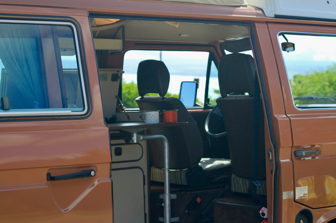 Experience road trip freedom! This cozy RV rental camper van, side door open, reveals its inviting interior and scenic outdoor view.
