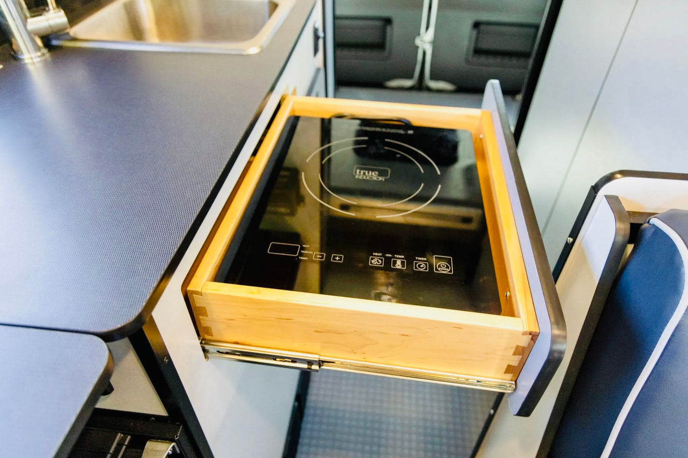 Compact kitchen in an RV rental, featuring a pull-out drawer with a True Induction cooktop for space-saving cooking.