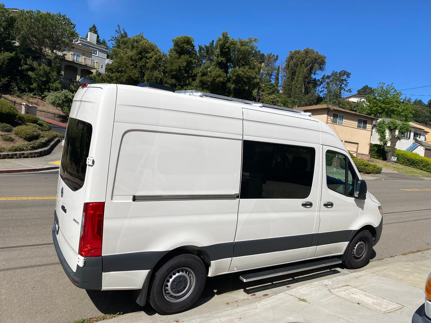 White Sprinter camper van, great for an rv rental, parked on a sunny residential street. Tinted windows & roof features visible.