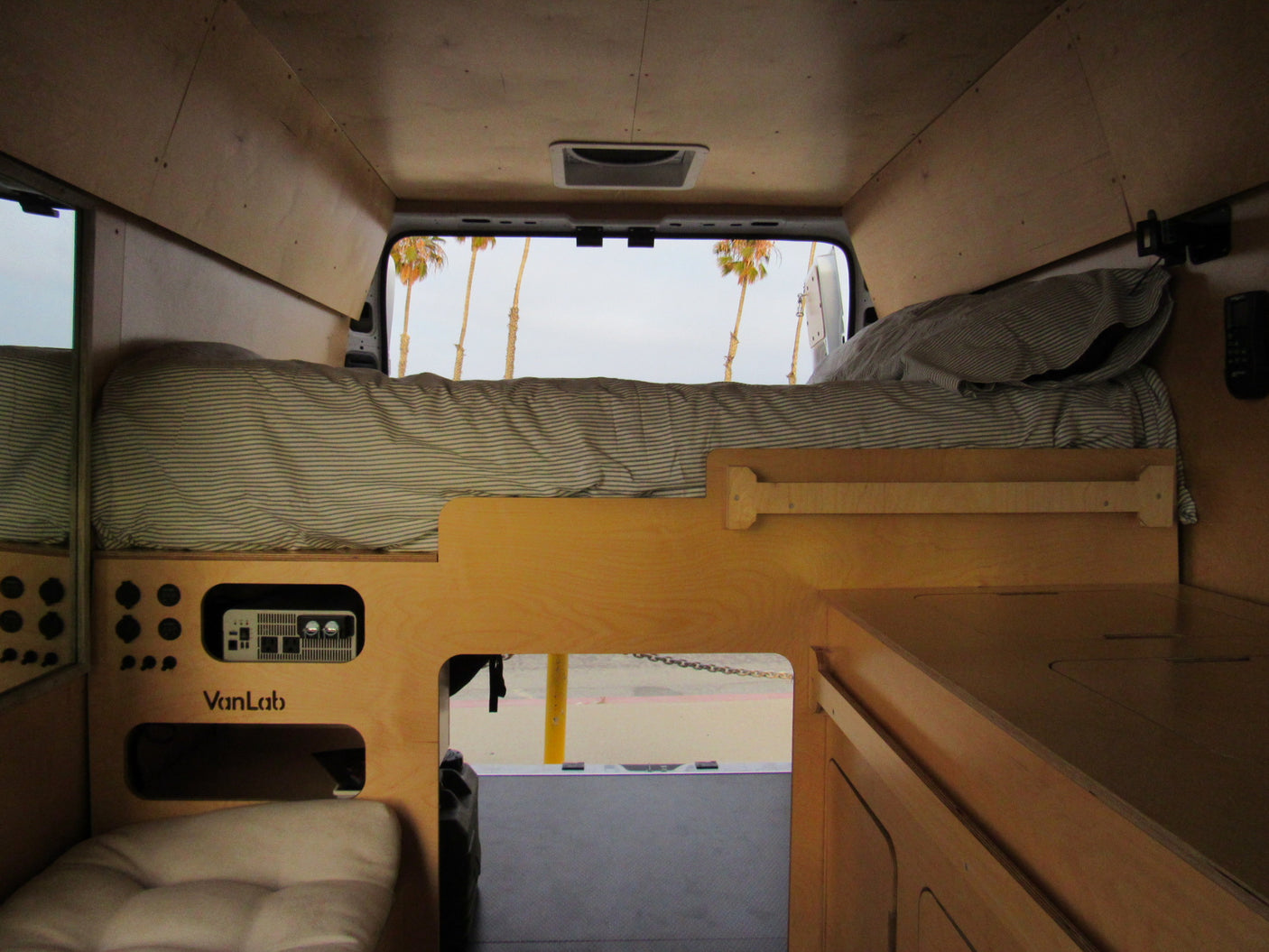 Inside a custom **rv rental** camper van: wooden interior, comfy bed, power hub, and views of palm trees.