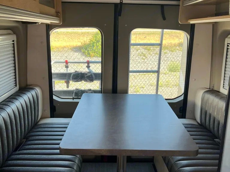 RV rental interior: comfy dinette with upholstered benches, large rear windows showing a fenced outdoor area.